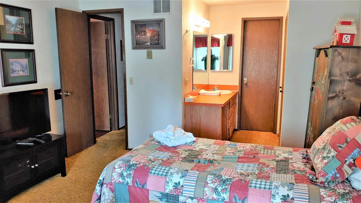 A bedroom with a plush bed adorned with a quilt, a vanity area for getting ready, and a TV. The space feels private and inviting, with soft lighting and thoughtful furnishings.
