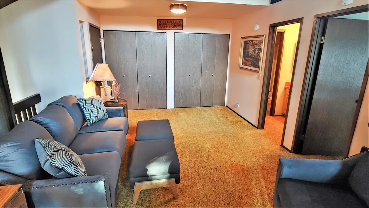 An inviting living room scene with a blue couch, wooden lamp, wall art, and spacious closets. The mood is cozy and relaxed, ideal for unwinding with friends, reading, or catching a movie—activities detailed in the section's retreat narrative.