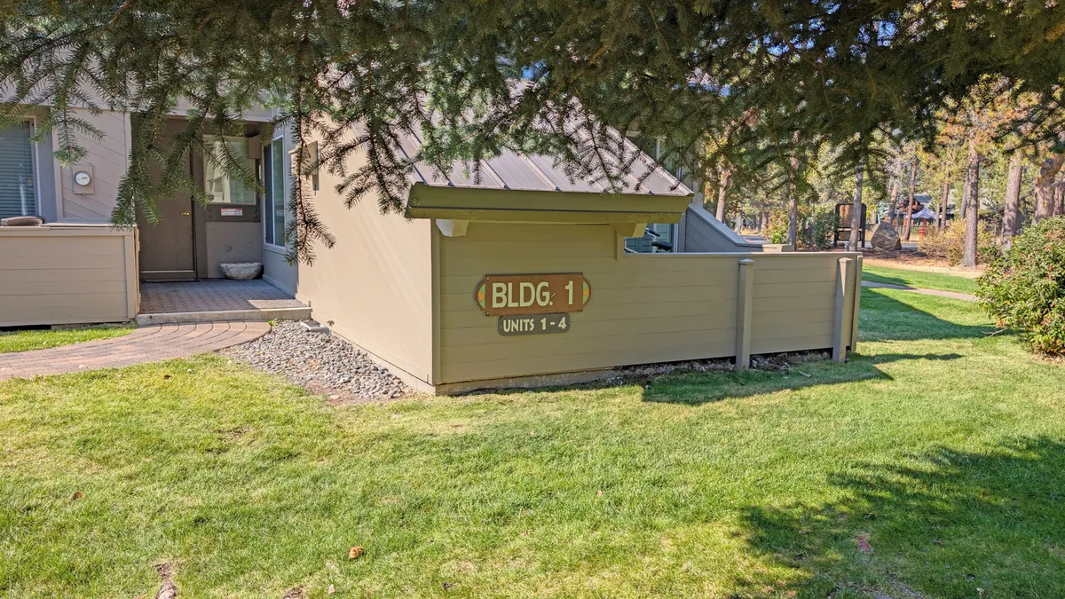 This exterior image features the front entrance to a community building, with a clear building sign ('BLDG. 1'), a landscaped lawn, and a welcoming walkway. The entrance area suggests an inviting and accessible environment for visitors and residents alike.
