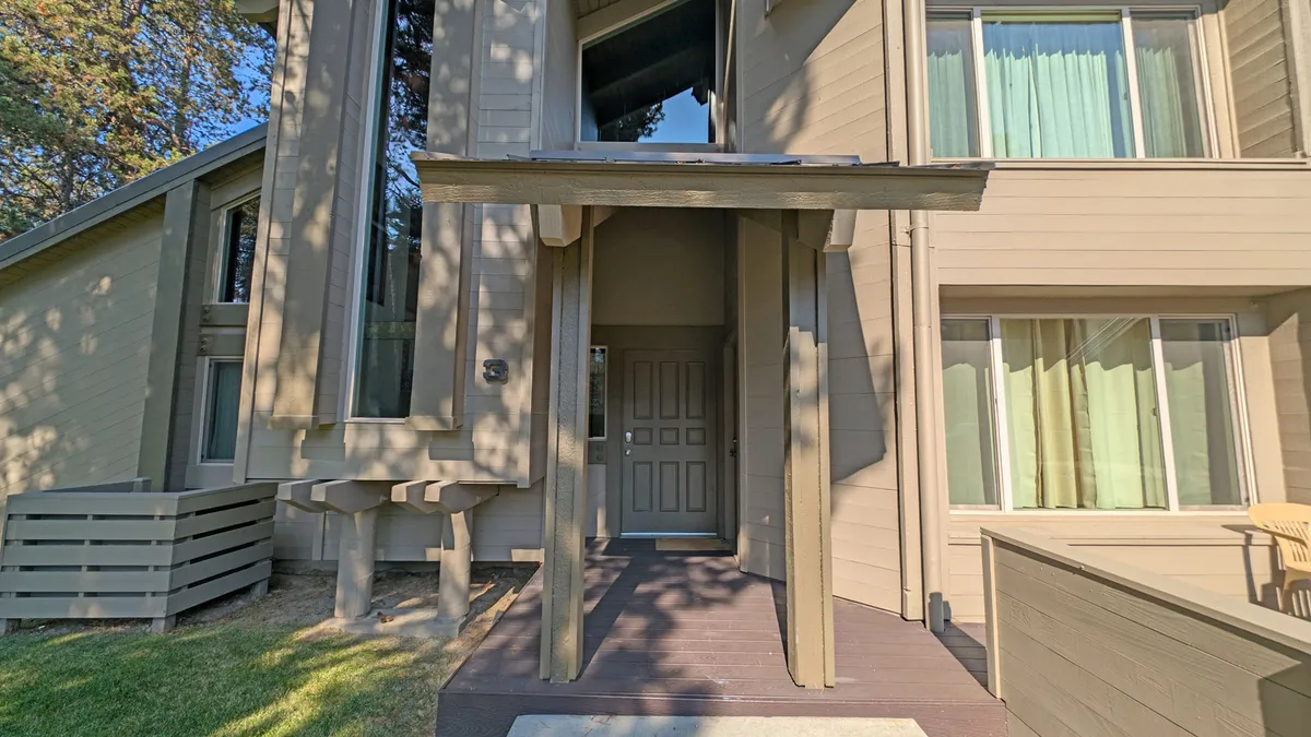 A welcoming exterior of the condo with entrance awning, large windows, and a patio seating area where guests can relax and socialize outdoors.