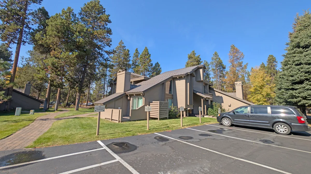 An inviting exterior shot of the main building surrounded by trees, open lawn, and spaces for outdoor gatherings or nature walks. The calm setting suggests both activity and relaxation within a natural environment.