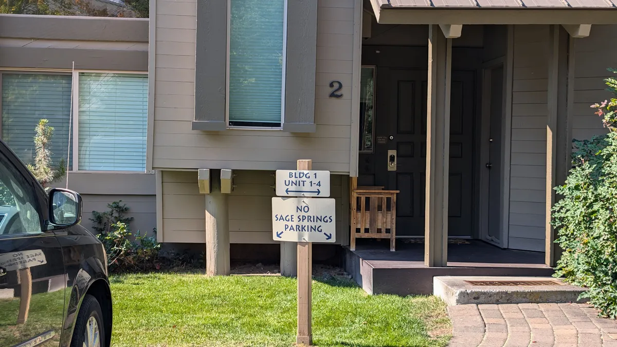 This exterior photo focuses on the condo's front door, welcoming signage, well-kept landscaping, and hints at the communal pathways outside. It sets a friendly, approachable tone and illustrates the property’s accessibility within the neighborhood.