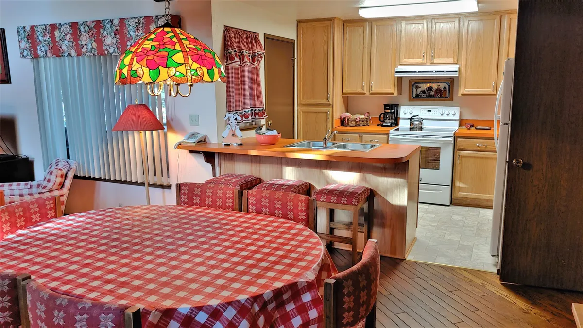 A classic retro kitchen and dining nook, with a checkered tablecloth, stained glass lamp, and open kitchen area. The space feels cheerful and social, ideal for shared meals or cooking together after enjoying the resort amenities.